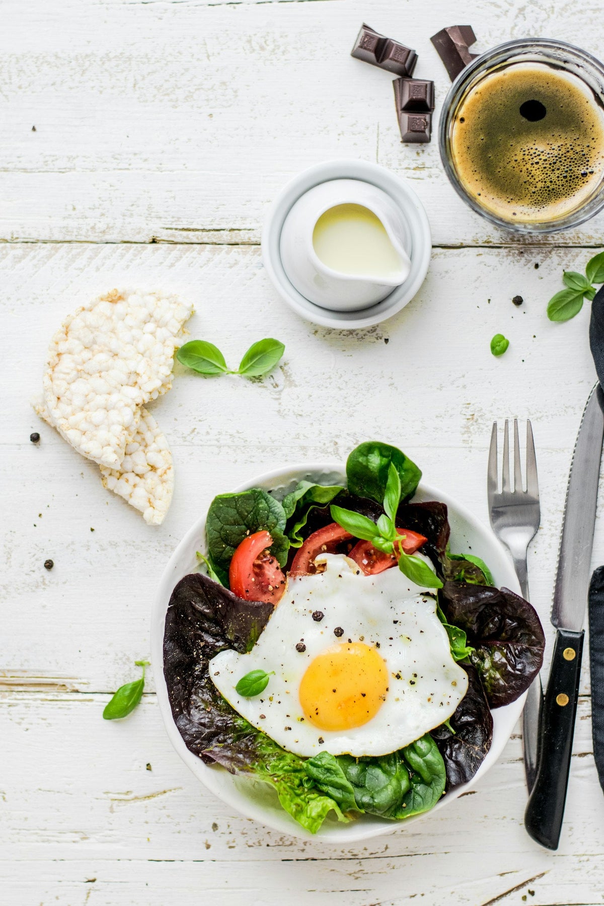 Fried egg with leafy salad, rice cakes and coffee on a white wooden table